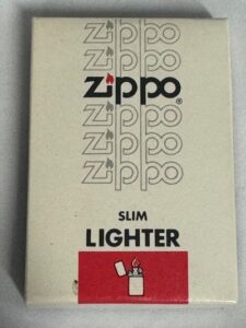 Beige Zippo Slim Lighter packaging with repeating Zippo logos and a red lower panel featuring a white lighter icon. 